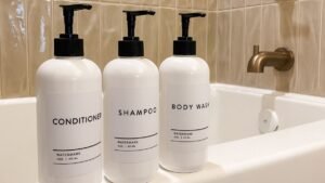 Three white pump bottles labeled Conditioner, Shampoo and Body Wash on a bathtub ledge