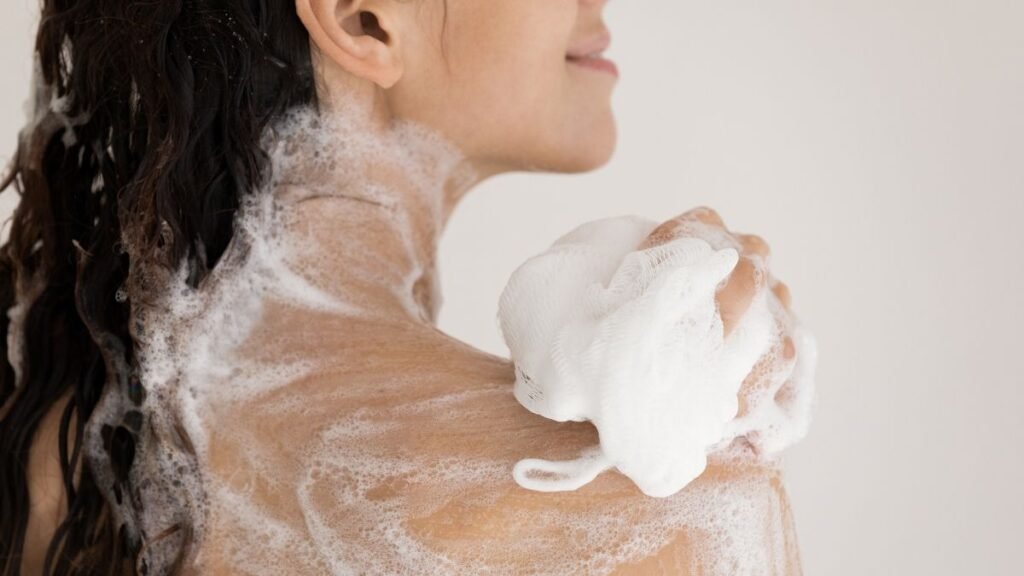 Woman lathering her shoulder with a white shower pouf